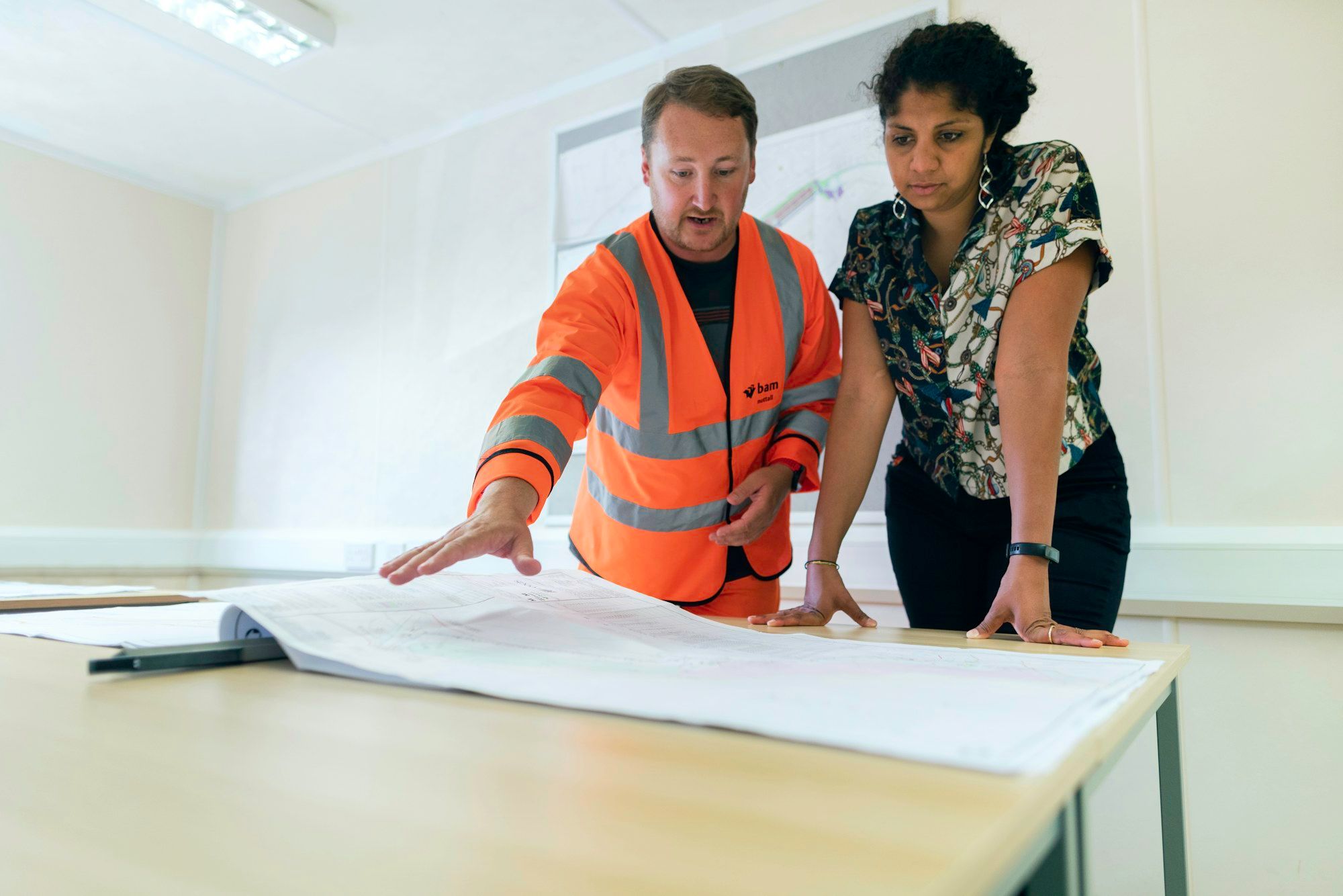 Inżynier w kamizelce ostrzegawczej i projektantka omawiają rysunki techniczne